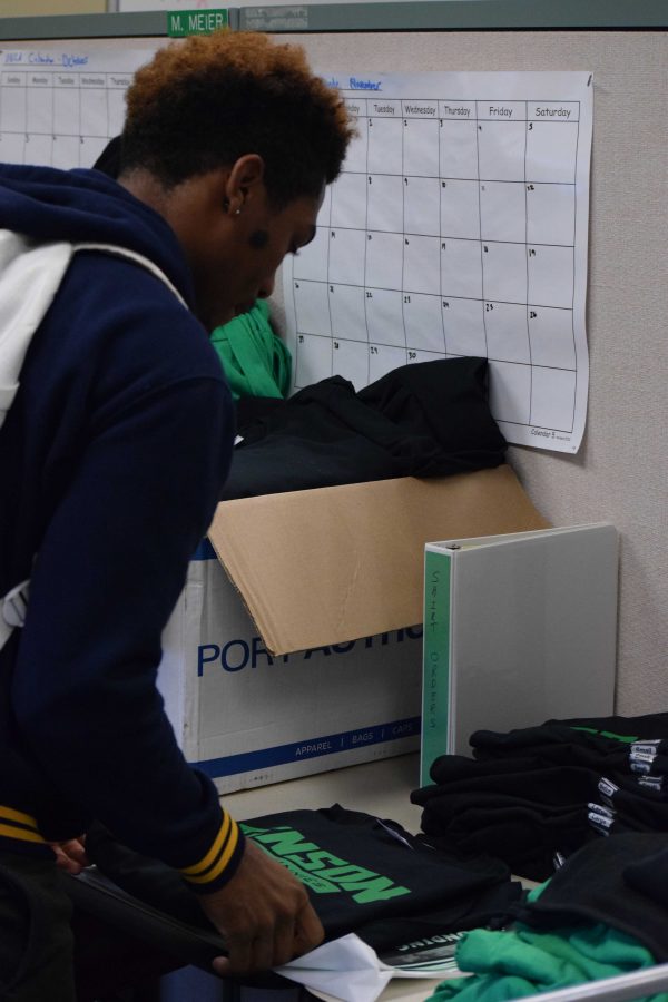 Senior Mario Stephmathews organizes a few shirts in the school store. He is making sure everything is in order before leaving.